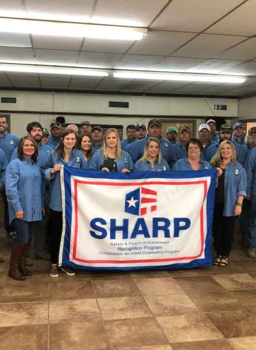 Oak River Farms employees holding a flag commemorating their SHARP status